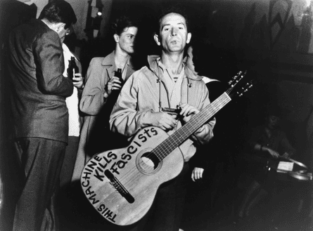 Woody Guthrie with “This Machine Kills Fascist” guitar and harmonica, circa 1941