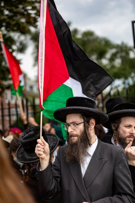 Jewish men with long brown beards, flat-topped, wide-brimmed black hats, black blazers and white shirts hold Palestinian flags.