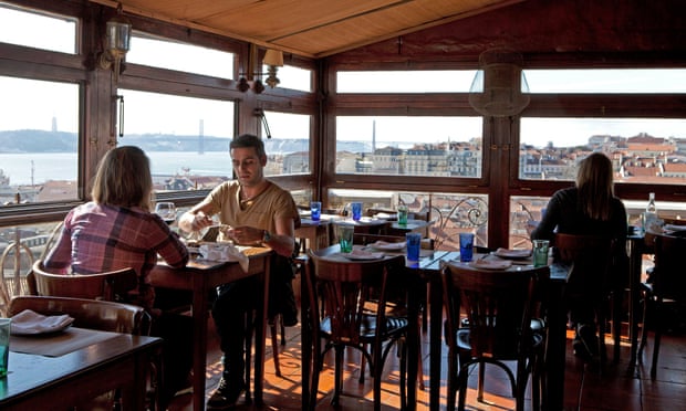 A couple dine in front of a window looking out on the Tagus river at Chapito restaurant, Alfama, Lisbon, Portugal.