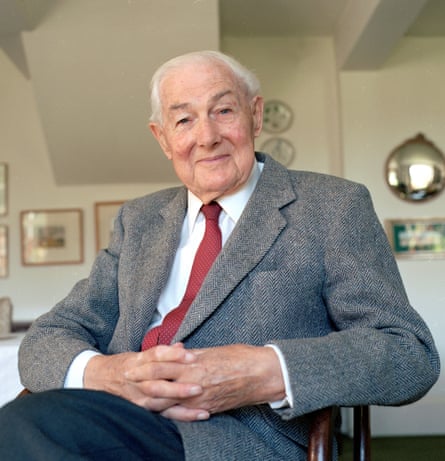 An elderly man in a grey suit smiles at the camera