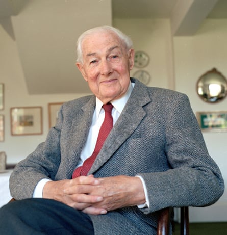 An elderly man in a grey suit smiles at the camera