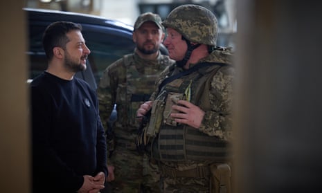 Zelenskiy in a dark sweater speaking to a soldier in combat fatigues.