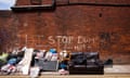 Ashton-under-Lyne in Greater Manchester: view of a brick wall with fly-tipped rubbish in front of it, including broken furniture and a leather sofa. Graffiti on the wall reads Stop Dumping Here, Grass, and Rat.