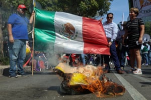 people hold a Mexican flag outside while a Trump piñata burns on the ground