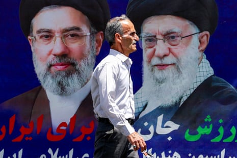 A man walks past a large banner depicting Iran’s current supreme leader Mojtaba Khamenei and his predecessor and late father Ali Khamenei along a street in Tehran.