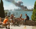 Young people relax during their lunch break along the East River while a huge plume of smoke rises from Lower Manhattan after the attack on the World Trade Center.