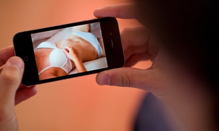 A young man holds a smartphone displaying an erotic photo of a young woman