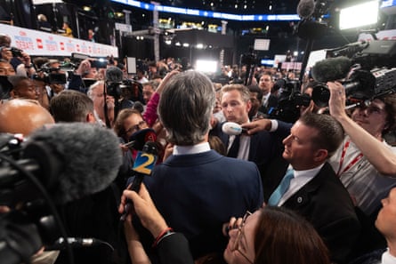 people with cameras and microphones surround man in blue suit
