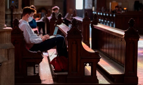 A student wearing a protective face mask studies on a computer as he sits on a pew at the Votive Church in Vienna,