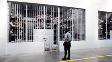 Guard watching prisoners pinch shaven heads sitting connected multi-level bunks