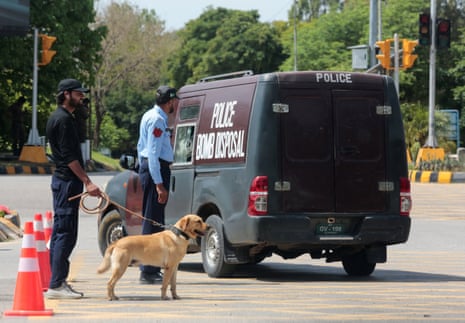 दो सुरक्षा अधिकारी एक कुत्ते के साथ पुलिस बम निरोधक वैन के बगल में खड़े हैं।