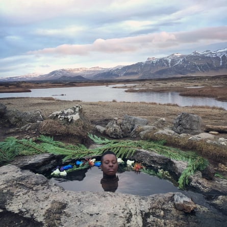 A man immersed up to his neck in a rock pool by a fjord with flowers around him