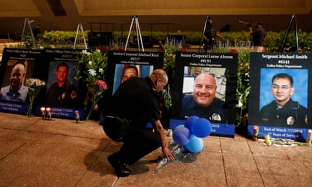 A Dallas police officer picks up balloons and flowers in front of images of the five officers killed.