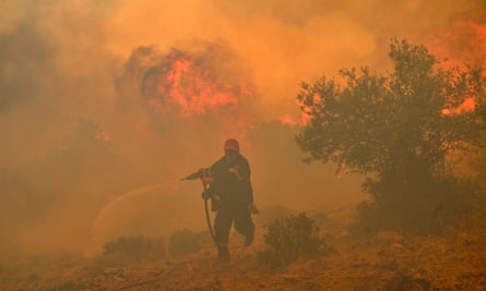A firefighter runs while spraying a hose at fire and smoke among trees and scrubland