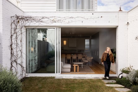 View from the back courtyard of a townhouse, looking into a living area with an open sliding door and a woman entering the yard