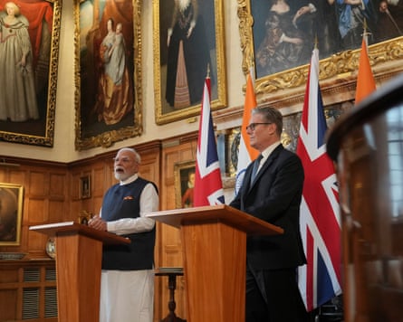 they stand at podiums with the Indian and union jack flags behind them. Large historic portrait paintings hang on the walls.