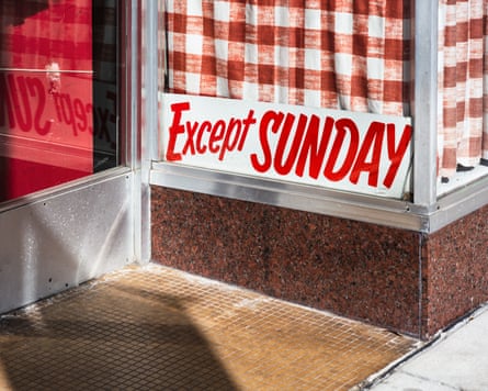 A sign reading ‘Except Sunday’ in the window of a cafe, with red check curtains behind it