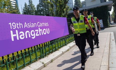Security guards walk by a poster of 19th Hangzhou Asian Games 