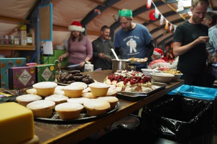 A Christmas spread of festive food on a table, with people wearing Christmas hats gathered round