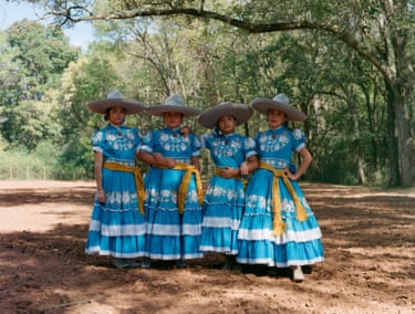 Four women in tradition dress and hats pose in the shade of a tree