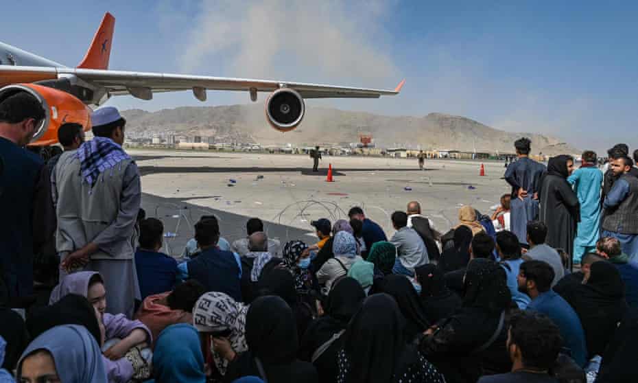 Afghan people sit on the tarmac as they hope to leave Kabul international airport on Monday