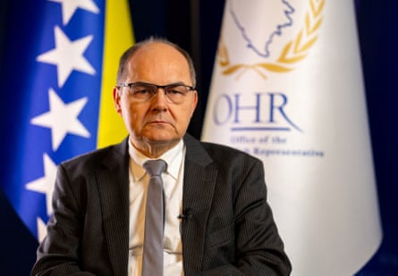 Christian Schmidt sits formally in front of flags, wearing a suit and tie and looking stern.