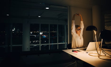 Woman stretching her arms while working late in dark office