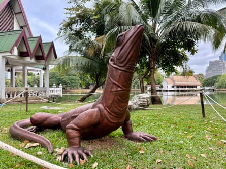 A bronze statue of a water monitor lizard on the grass by a palm tree