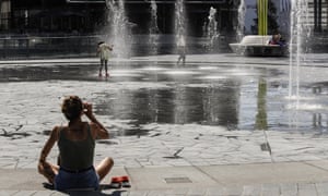 A woman drinks as children cool off in a public fountain in Milan, Italy, on 31 July.