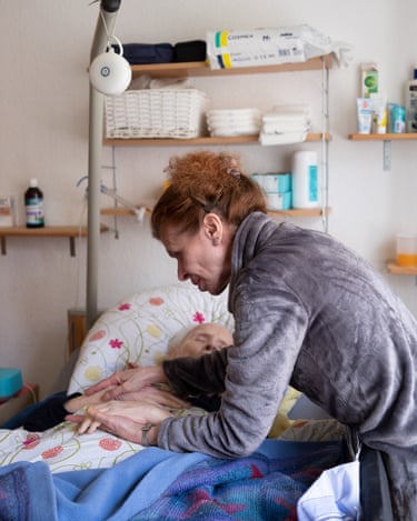 Mrs Schiller leans over the bed of a Mr Schiller who appears to be sleeping