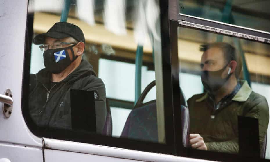 people on bus with masks, one with scottish flag on it