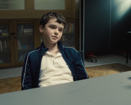 Owen Cooper sits behind a green desk in a scene from Adolescence.