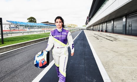 Jamie Chadwick in her racing gear and holding her helmet, walking on the track at Silverstone.