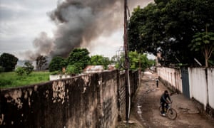 A man rides his bike as smoke rises from a fire at the independent national electoral commission’s (CENI) warehouse in Kinshasa.