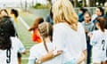 Mother embracing young female football player on sidelines after game