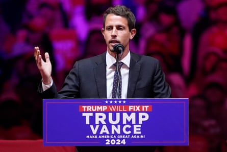 man gestures behind podium that says ‘trump vance’