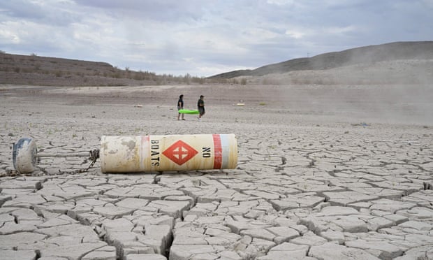 A buoy that reads “no boats” lays on cracked dry earth where water once was, as people carry out a boat at Lake Mead, Nevada on 23 July 2022.