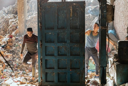 رجلان يقفان وسط أكوام من نفايات الورق والكرتون، جاهزة للتحميل في ضاغط لضغطها إلى كتل مدمجة