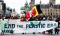 Protesters walk down a street carrying a banner reading 'End the plastic era' with government buildings behind them