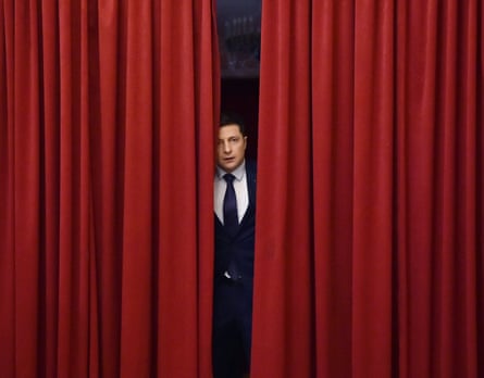 Volodymyr Zelenskyy looks out from between two red stage curtains