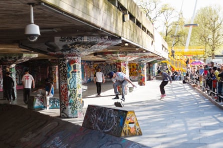 People watch skateboarders beneath concrete structure