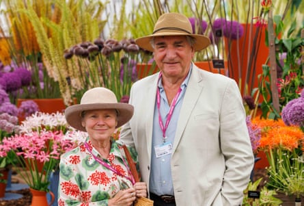 A woman in a floral dress wearing a straw hat, and a man in a beige jacket and light blue shirt wearing a hat