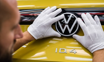 A worker with gloved hands places a VW badge on a yellow car