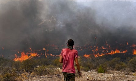 A person with their back to the camera looks out at the panorama of fire and smoke in front of them