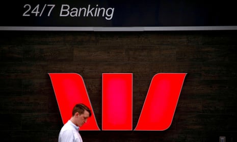 A pedestrian looks at his phone as he walks past Australia's Westpac Banking Corp logo, located outside a branch in central Sydney, Australia.
