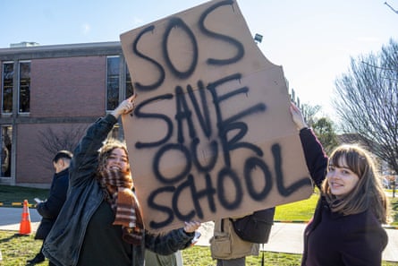 people hold a sign that reads ‘SOS save our school’