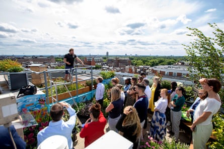 A man standing next to a beehive speaks to a group of people on the rooftop of Park House