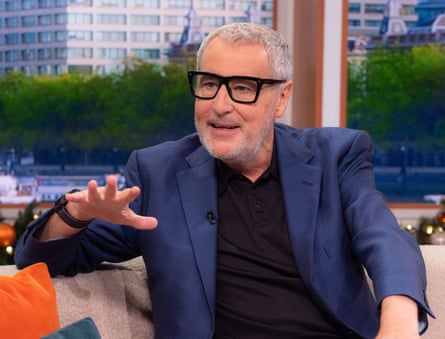 On the sofa of Good Morning Britain, wearing a black T-shirt under a blue suit jacket and wearing black-rimmed glasses, Dermot Murnaghan talks animatedly to his interviewer