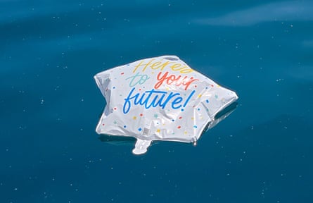 A plastic star-shaped balloon, partly deflated, with a message “here’s to your future!” floating on a lake