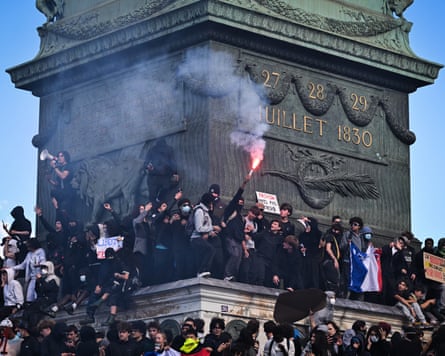 Dozens of protesters stand on the plinth of the July Column in Paris, one holding up a lit flare